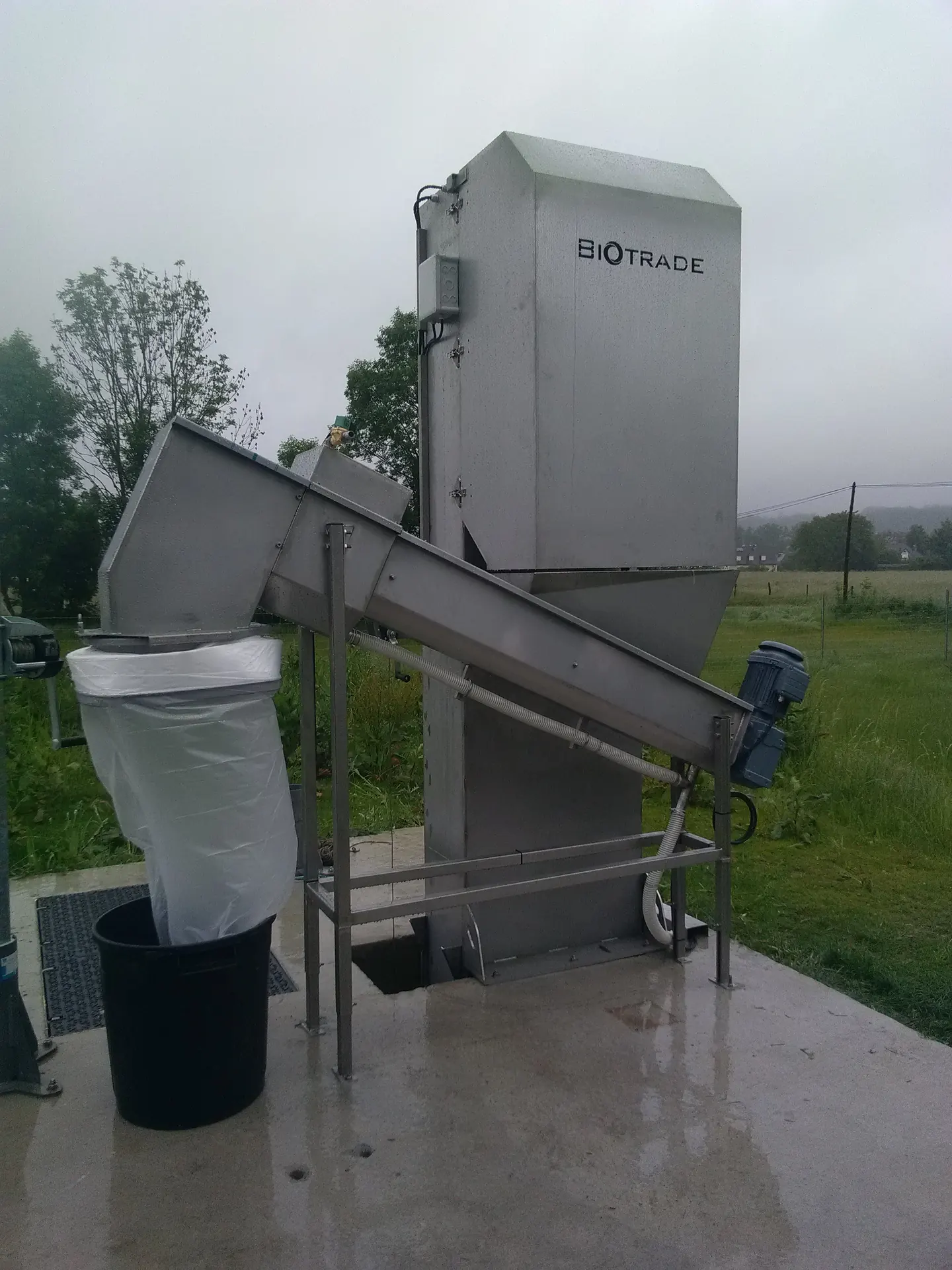 Vis de compactage Biotrade DV 800 installée en station d'épuration rurale par temps de pluie avec sac de collecte Longopac et bac roulant