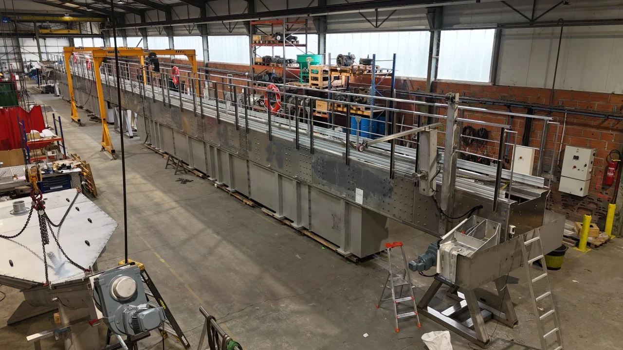 Vue en hauteur de l'atelier de fabrication BioTrade avec une machine de traitement de l'eau en acier inoxydable et des ponts roulants jaunes