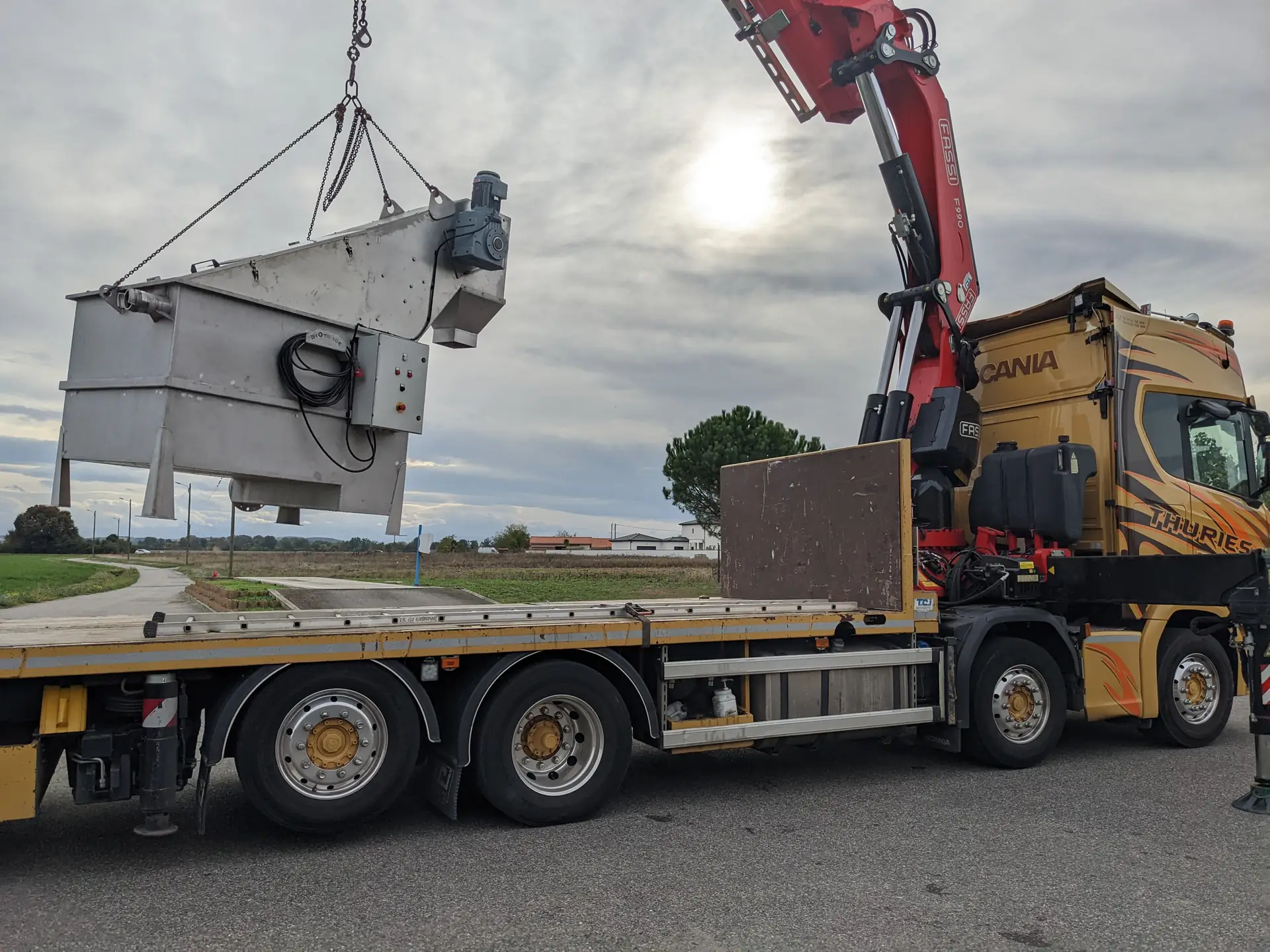 Dégrilleur matières de vidange Biotrade suspendu par grue Fassi au-dessus du plateau d'un camion Scania Thuries lors de la mise en place