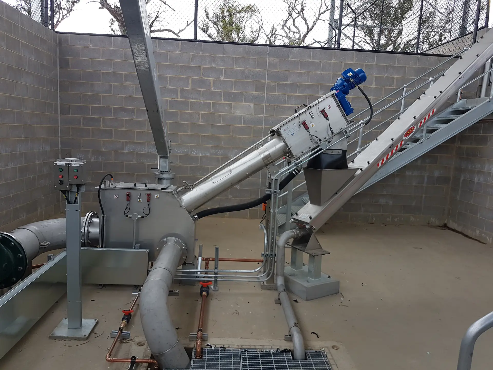 Tamis à vis en caisson inox Biotrade installé sur chantier avec vis compacteuse inclinée, motoréducteur bleu et réseau de tuyauteries