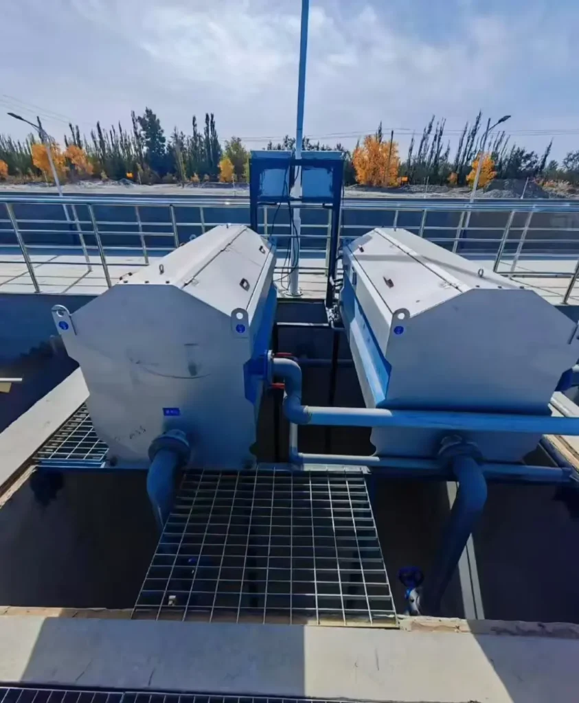 Deux filtres tambour Biotrade installés en parallèle sur une station d'épuration en extérieur, pour le traitement tertiaire des eaux, avec passerelle caillebotis et paysage d'automne en arrière-plan