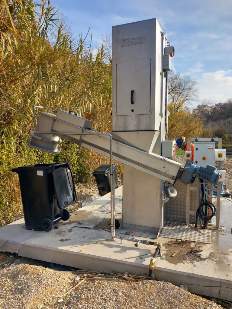 Technicien Biotrade procédant à la mise en service d'un dégrilleur BioScreen BV sur un chantier de station d'épuration, avec convoyeur et coffret électrique