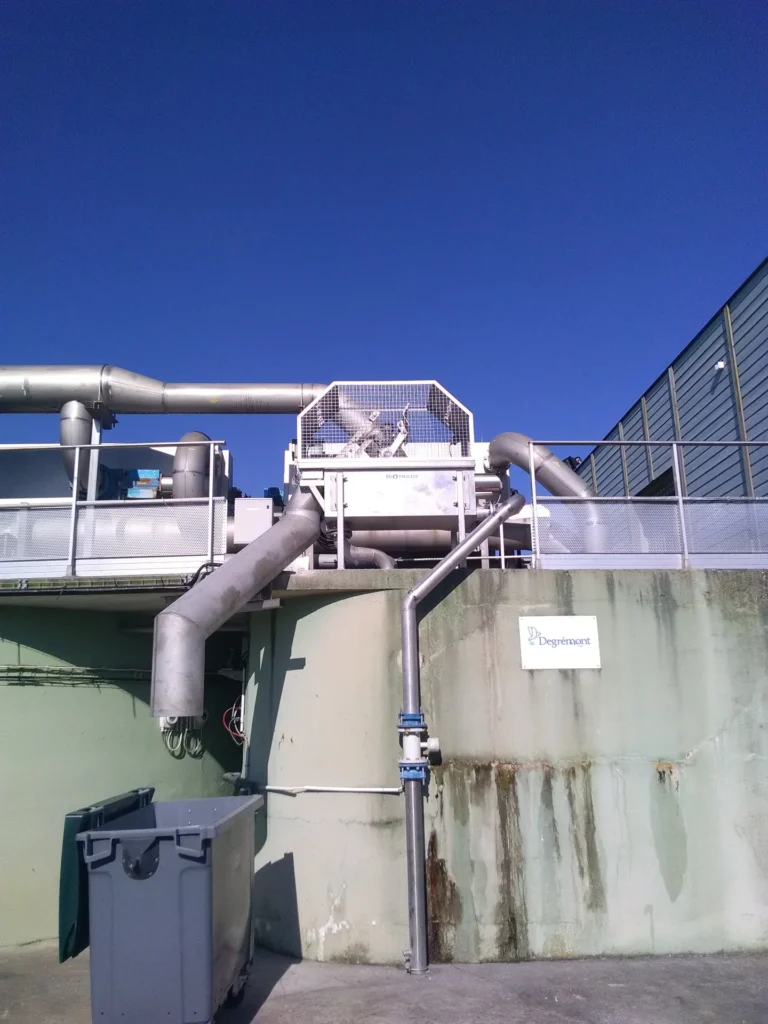 Dégrilleur BioScreen DC Biotrade installé en hauteur à l'extérieur d'un ouvrage de béton, avec réseau de canalisations inox et ciel bleu