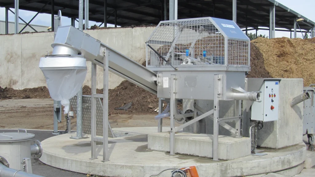 Dégrilleur BioScreen DC Biotrade installé sur un site de compostage ou de méthanisation, avec tas de matière organique et sac de collecte des refus