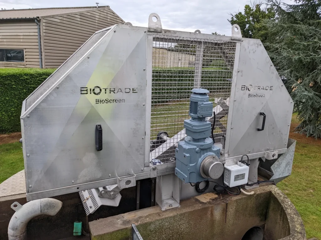 Vue frontale du dégrilleur BioScreen DC Biotrade avec logo, motoréducteur SEW central et grille de protection, installé sur un ouvrage béton extérieur
