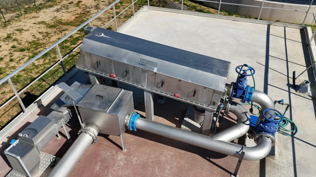 Vue aérienne du dégrilleur BioScreen TRI Biotrade avec tapis convoyeur et vannes bleues, installé sur une dalle béton de station d'épuration