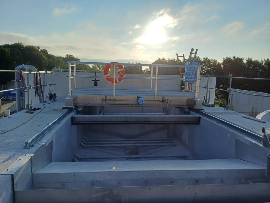 Pont baladeur Biotrade installé au-dessus d'un bassin de décantation rectangulaire béton dans le Morbihan, avec structure aluminium et soleil couchant en arrière-plan