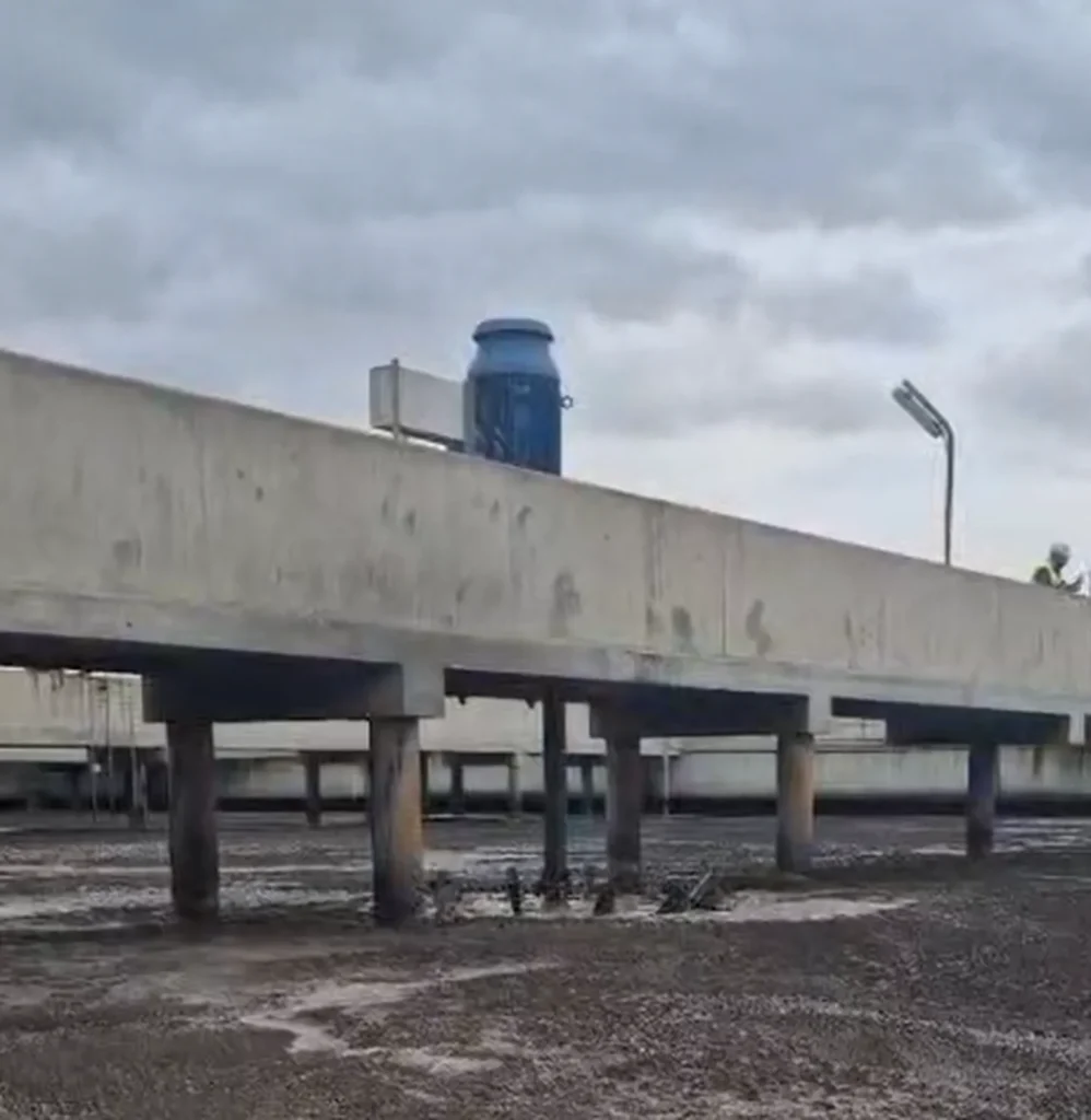 Turbine lente Biotrade à rotor acier grande puissance installée sur un pont-passerelle béton au-dessus d'un bassin de lagunage au Maroc, par temps nuageux